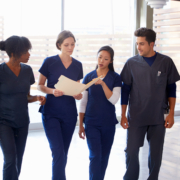 Healthcare,Colleagues,Discussing,Notes,In,Hospital,Corridor
