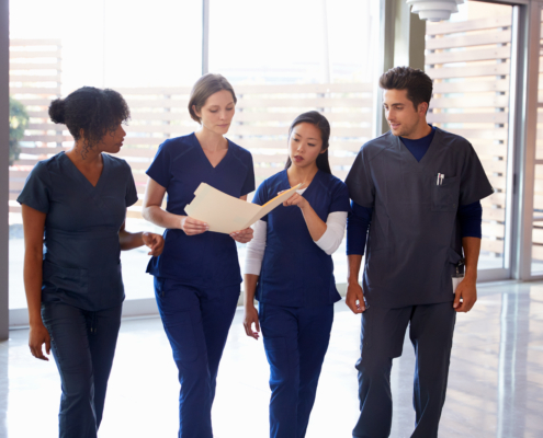 Healthcare,Colleagues,Discussing,Notes,In,Hospital,Corridor
