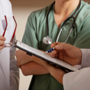 Midsection,Of,Doctor,Holding,Clipboard,While,Standing,With,Colleagues
