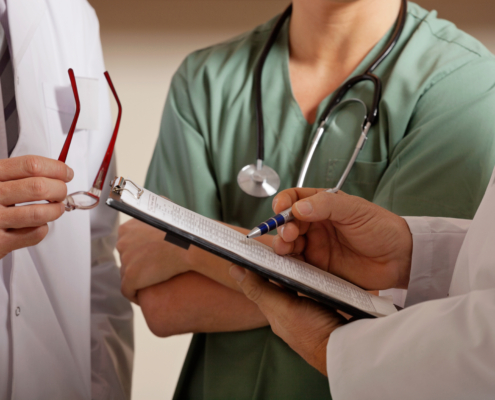 Midsection,Of,Doctor,Holding,Clipboard,While,Standing,With,Colleagues