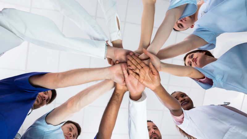 Low,Angle,View,Of,Doctor,Stacking,Hands,Together,In,Hospital