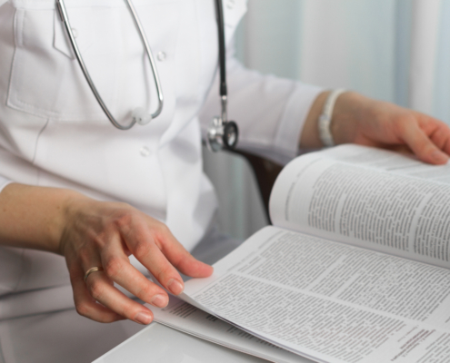 Hands,Of,A,Female,Doctor,Holding,A,Medical,Journal,In