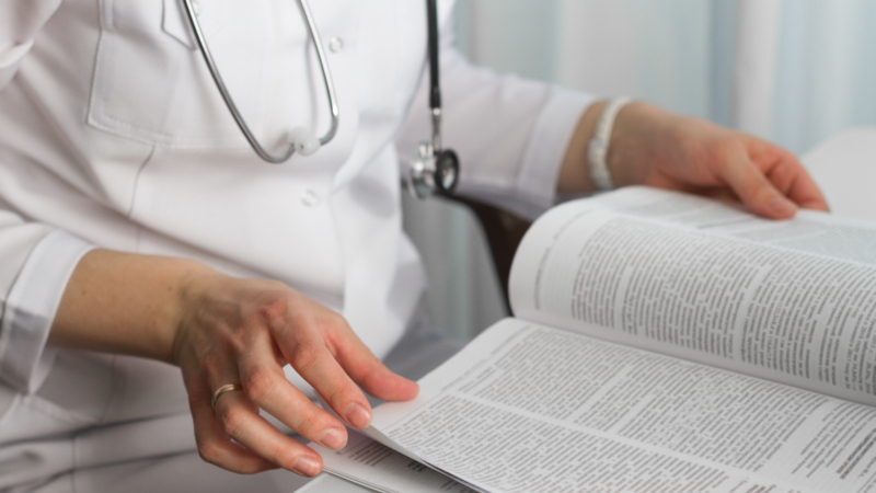Hands,Of,A,Female,Doctor,Holding,A,Medical,Journal,In