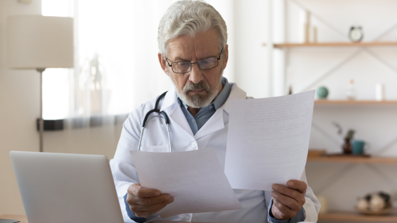 Serious,Professional,Senior,Elderly,Doctor,Doing,Paperwork,Checking,Medical,Documents