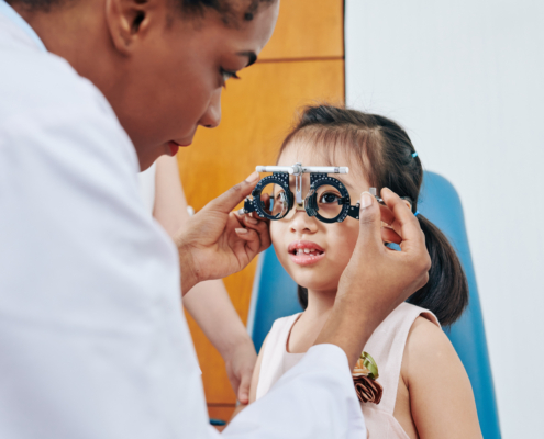 Pediatric,Optometrist,Helping,Little,Girl,To,Put,On,Test,Glasses
