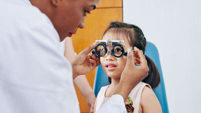 Pediatric,Optometrist,Helping,Little,Girl,To,Put,On,Test,Glasses