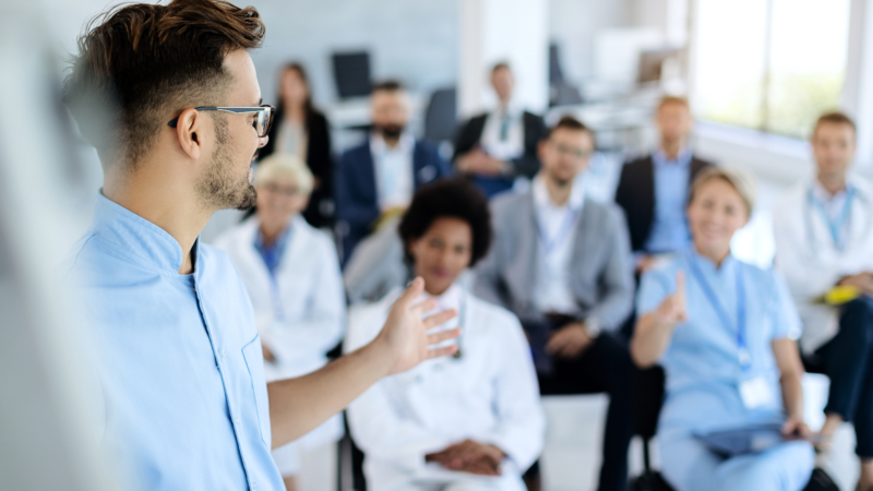 Young,Doctor,Talking,To,Group,Of,His,Colleagues,And,Business