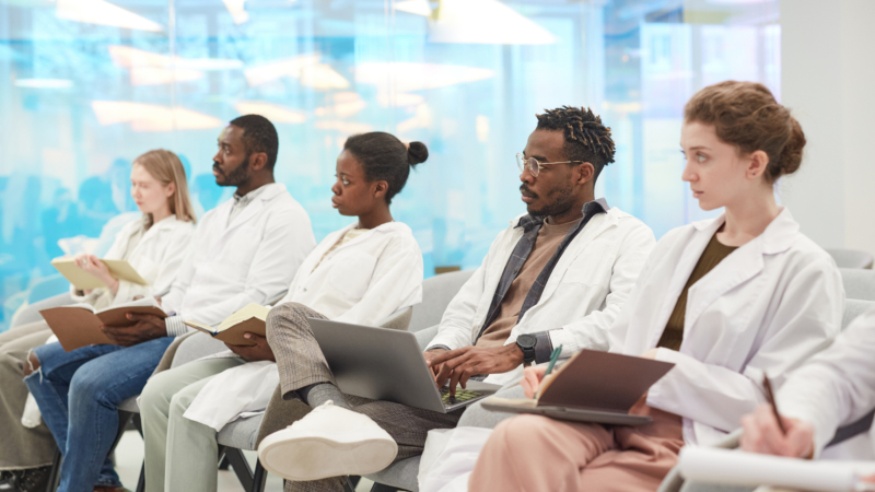 Multi-ethnic,Group,Of,People,Wearing,Lab,Coats,Sitting,In,Row
