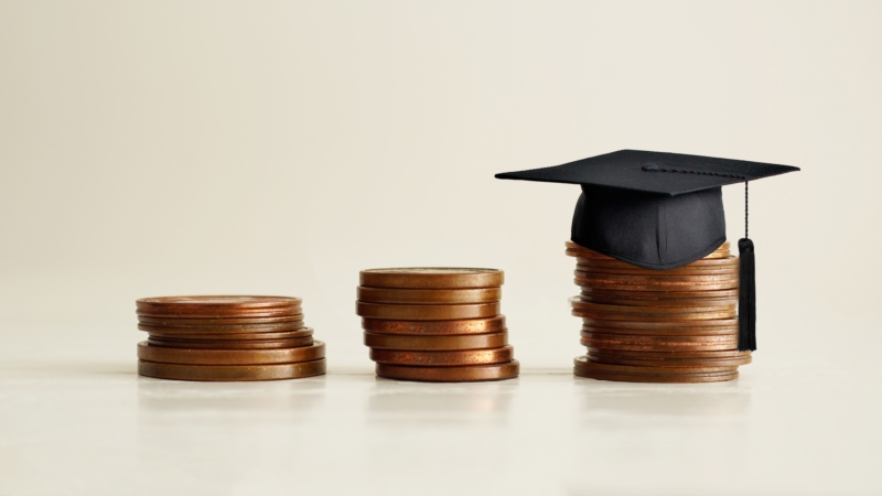 Black,Graduation,Cap,On,Stocks,Of,Coins,,Depicting,Strong,Effort