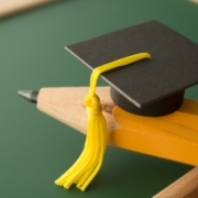 Small,Graduation,Cap,On,Pencil,With,Chalkboard,Background,In,Classroom.
