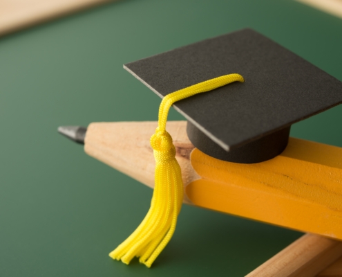 Small,Graduation,Cap,On,Pencil,With,Chalkboard,Background,In,Classroom.