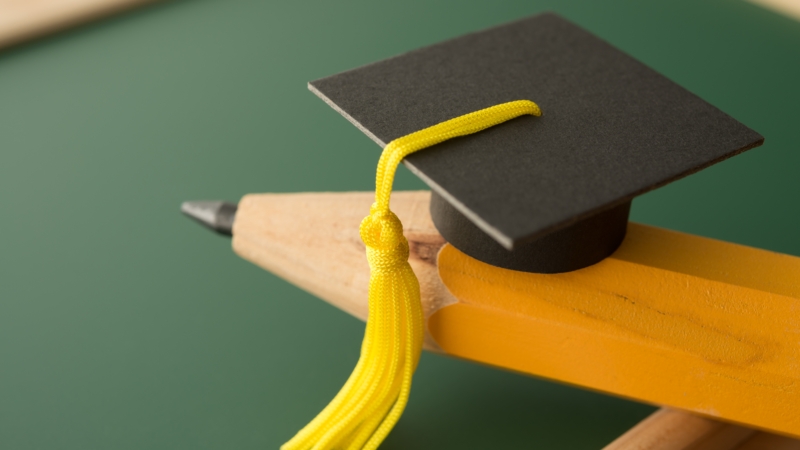 Small,Graduation,Cap,On,Pencil,With,Chalkboard,Background,In,Classroom.
