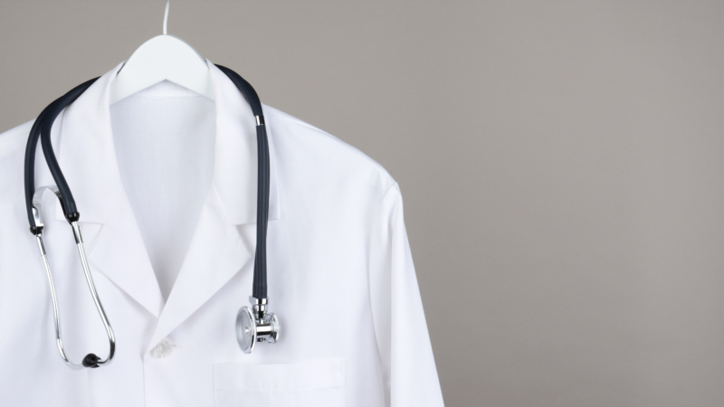 A,Doctor’s,Lab,Coat,And,Stethoscope,On,Hanger,Against,A