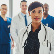 Confident,Female,Doctor,In,Front,Of,Team,,Looking,At,Camera